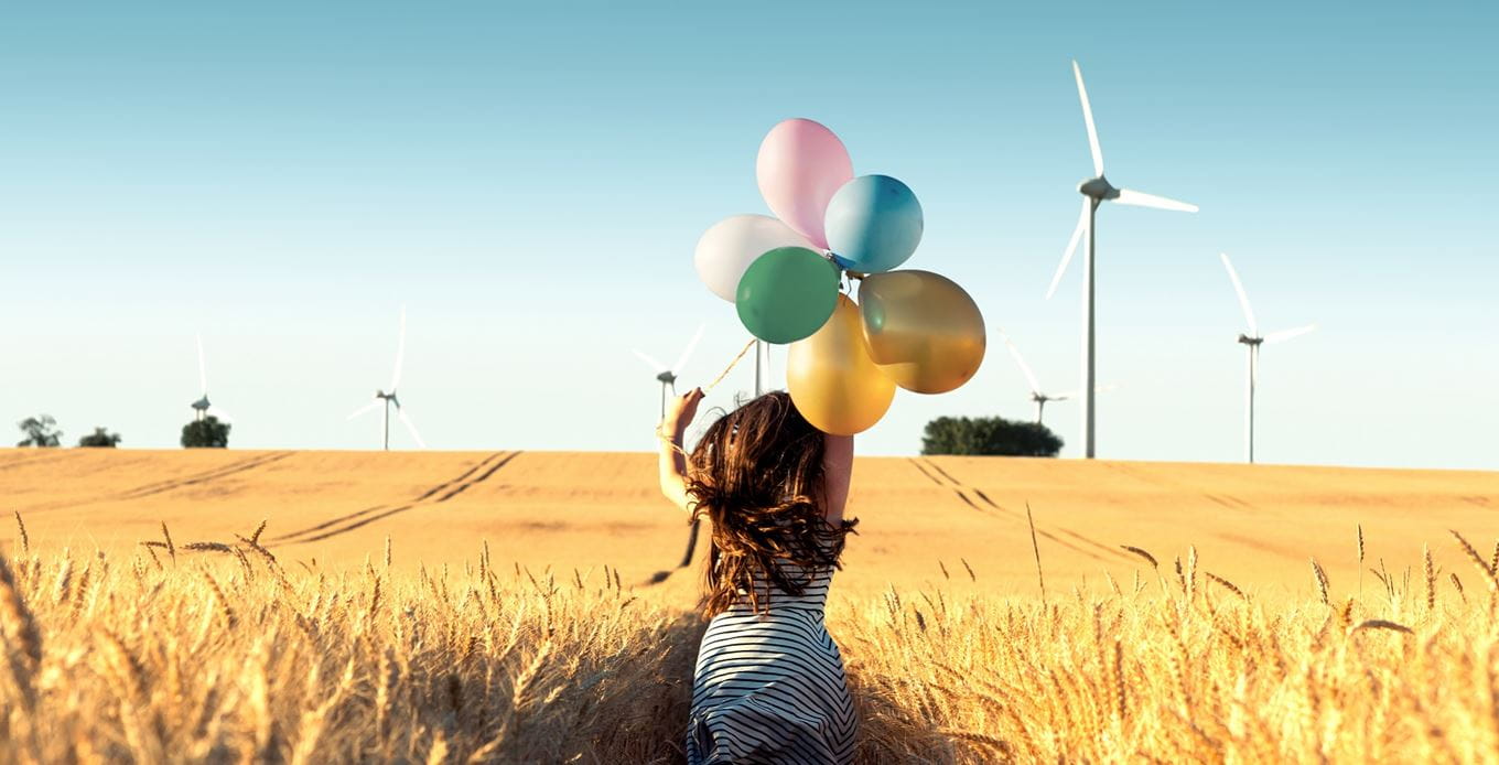 Girl with balloons running through windmill field